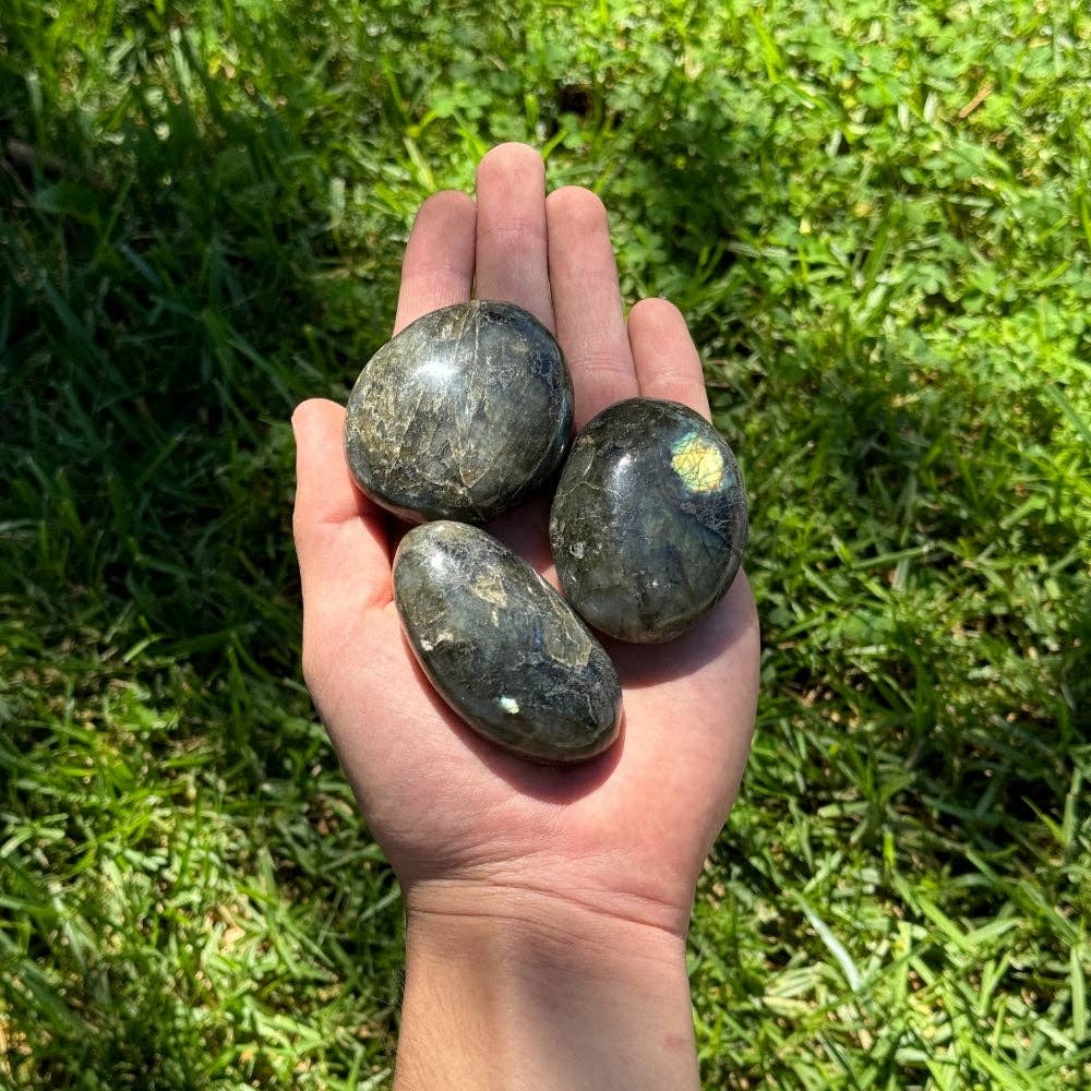 Hand holding three labradorite palm stones against a grassy background