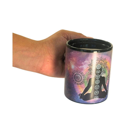 Hand holding a chakra mug with a mandala design and silhouette of a person on a white background