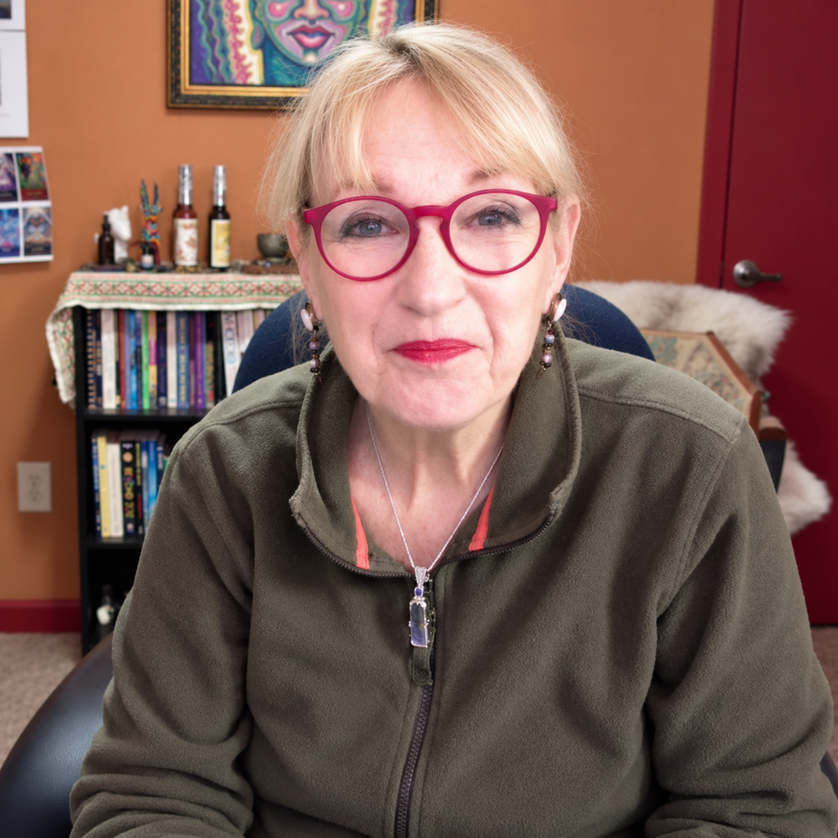 Katherine Skaggs, soul guide, visionary artist, spiritual teaching  wearing an olive green zip-up fleece jacket, sitting in a chair in a home office environment.