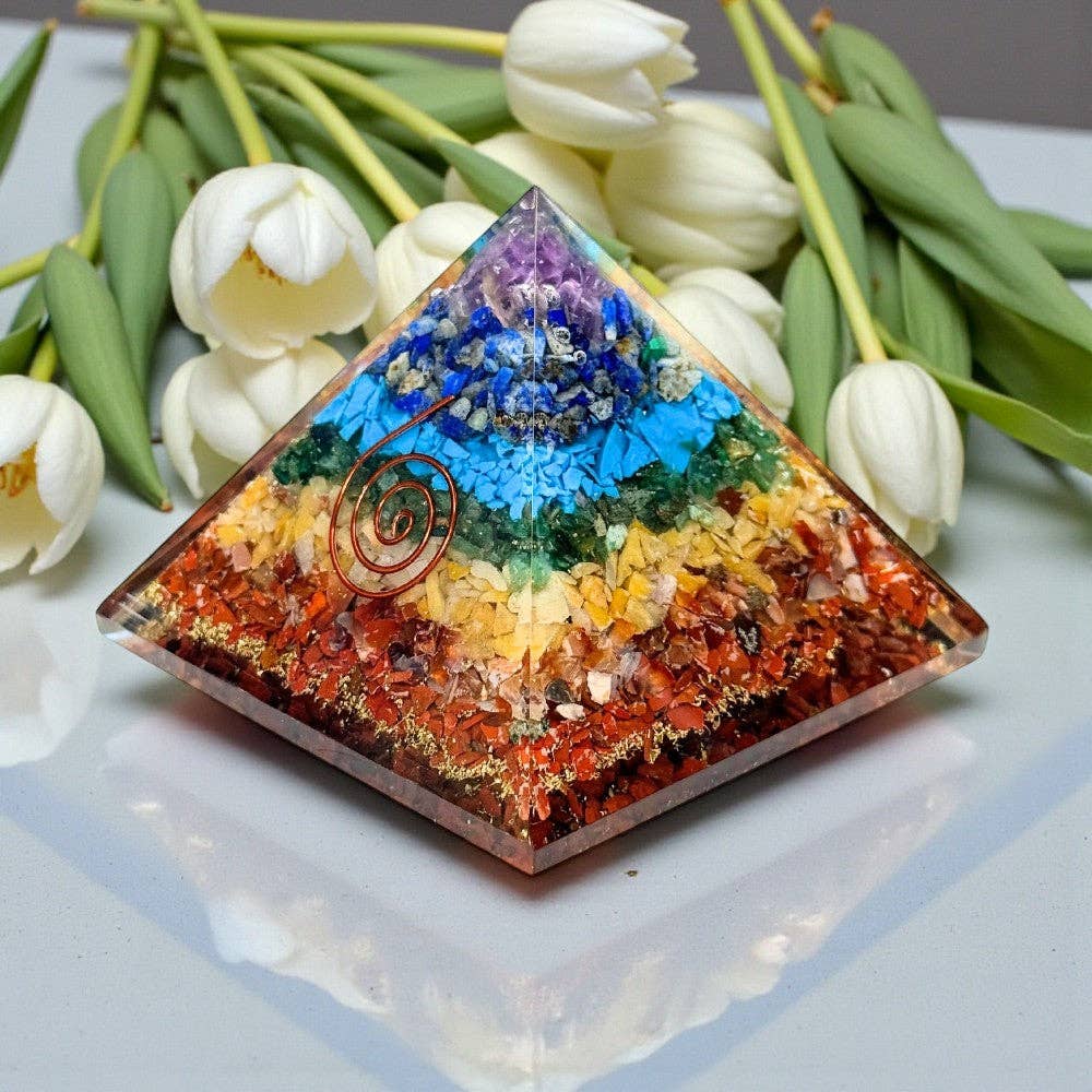Colorful pyramid-shaped crystal with chakra colors on a white surface with tulips in the background at KatherineSkaggs.com