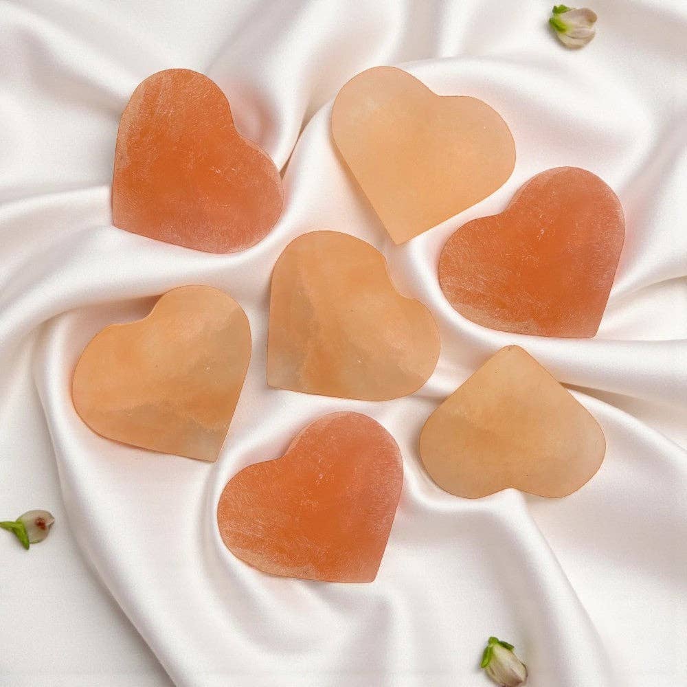 Heart-shaped peach selenite stones on a white fabric background at KatherineSkaggs.com
